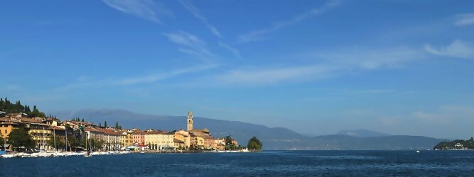 Trip Mietwagen beliebte Urlaubsziele am Gardasee -  Mit einer Fläche von 370 km² ist der Gardasee der größte See Italiens. Es liegt am Fuße der Alpen und erstreckt sich über drei Staaten: Lombardei, Venetien und Trentino. Die maximale Tiefe des Sees beträgt 346 m, er hat eine längliche Form und sein nördliches Ende ist sehr schmal. Dort ist der See von den Bergen der Gruppo di Baldo umgeben. Du trittst aus deinem gemütlichen Hotelzimmer und es begrüßt dich die warme italienische Sonne. Du blickst auf den atemberaubenden Gardasee, der in zahlreichen Blautönen schimmert - von tiefem Dunkelblau bis zu funkelndem Türkis. Majestätische Berge umgeben dich, während die Brise sanft deine Haut streichelt und der Duft von blühenden Zitronenbäumen deine Nase kitzelt. Du schlenderst die malerischen, engen Gassen entlang, vorbei an farbenfrohen, blumengeschmückten Häusern. Vereinzelt unterbricht das fröhliche Lachen der Einheimischen die friedvolle Stille. Du fühlst dich wie in einem Traum, der nicht enden will. Jeder Schritt führt dich zu neuen Entdeckungen und Abenteuern. Du probierst die köstliche italienische Küche mit ihren frischen Zutaten und verführerischen Aromen. Die Sonne geht langsam unter und taucht den Himmel in ein leuchtendes Orange-rot - ein spektakulärer Anblick.